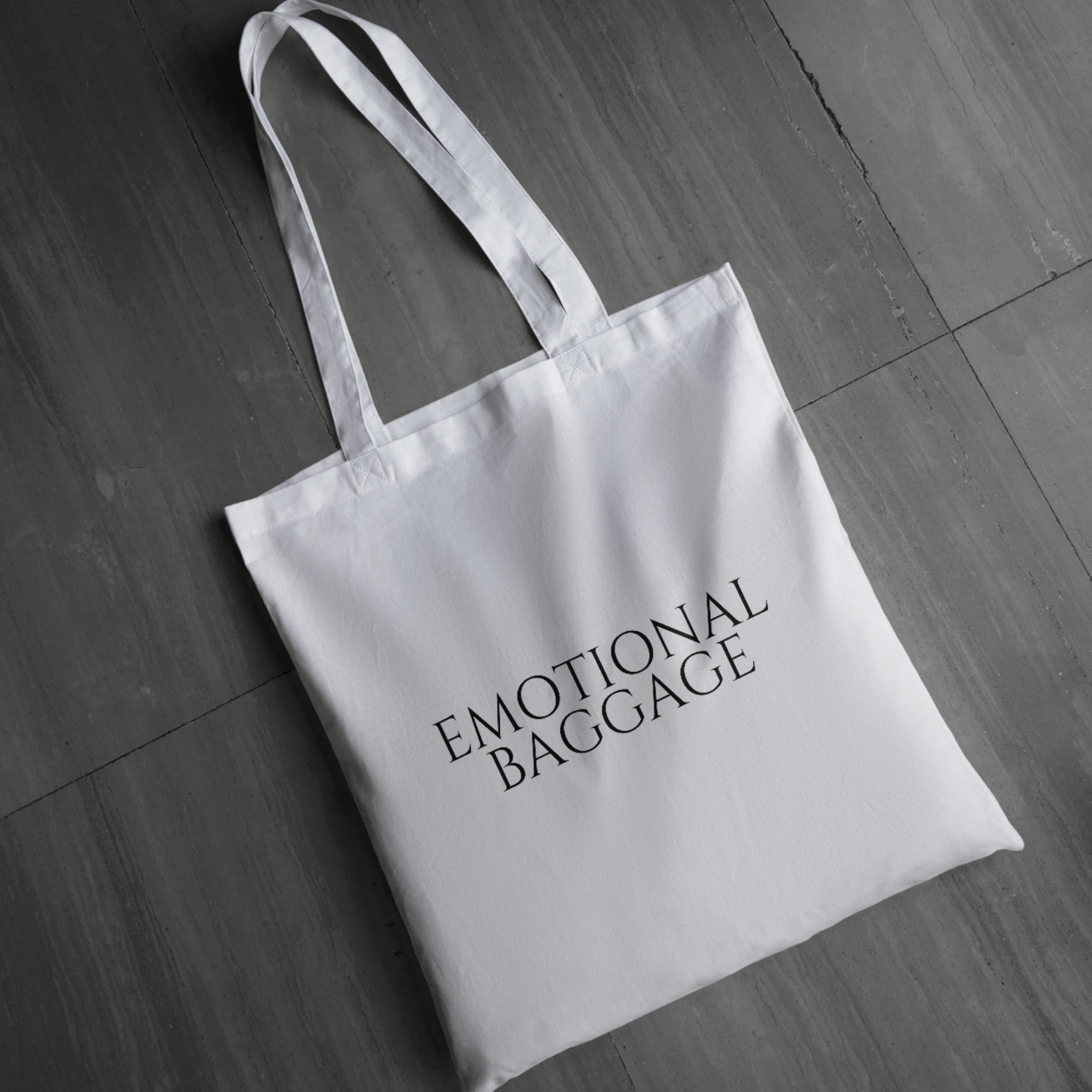 White canvas tote bag with “Emotional Baggage” minimalist text design